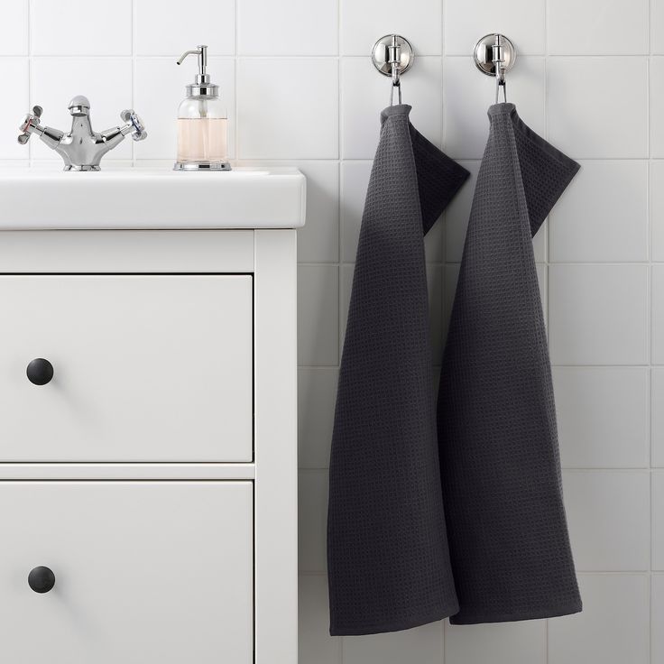 two black towels hanging on the wall next to a white cabinet and sink with faucet