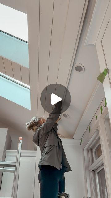 a woman is painting the ceiling in an office building with skylights and ladders