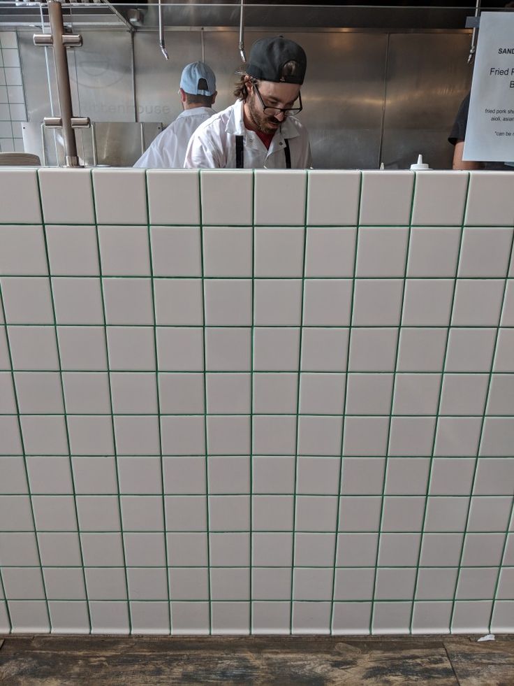 two men working in a commercial kitchen with tile on the wall and flooring behind them