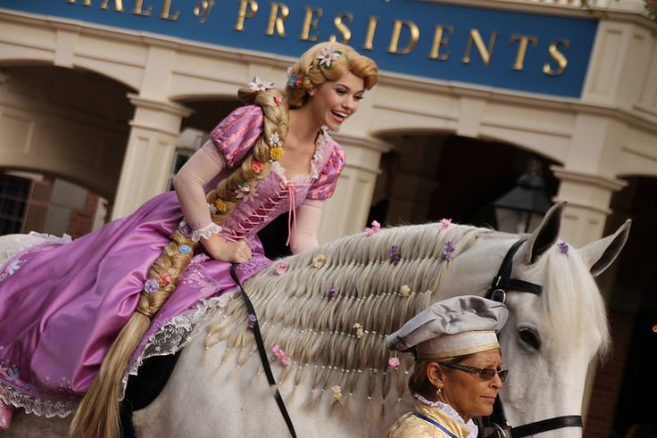 a woman riding on the back of a white horse next to a man in costume