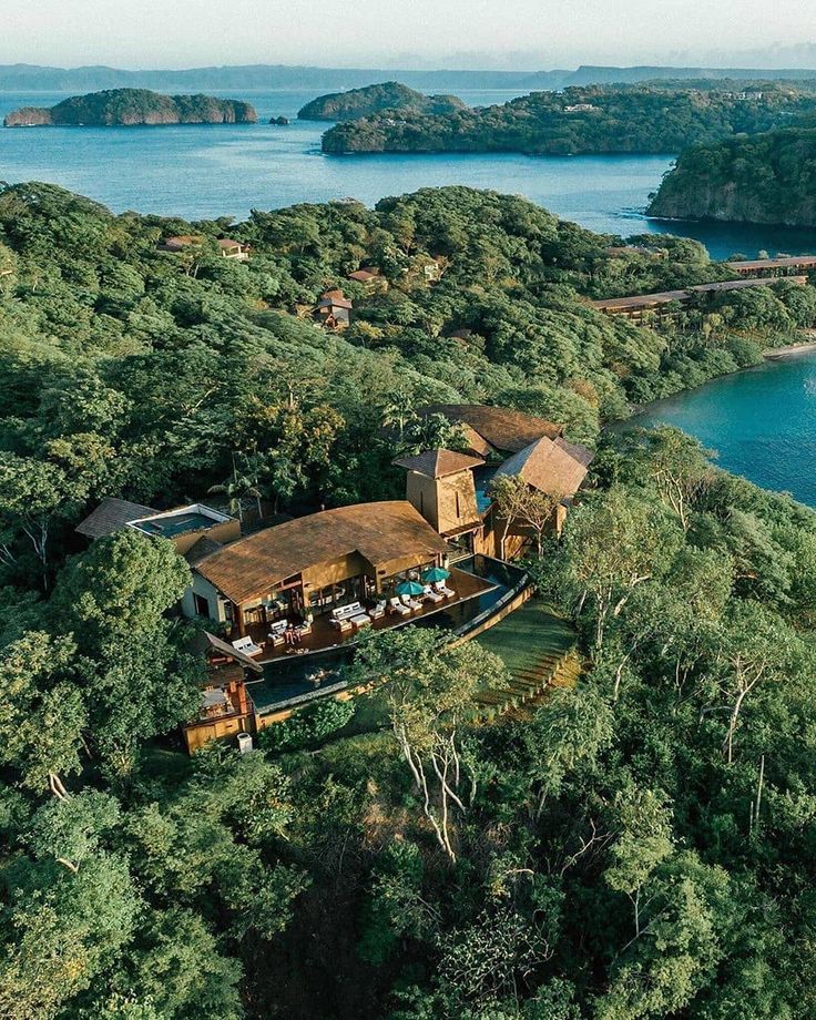 an aerial view of a house in the middle of trees with water and land around it