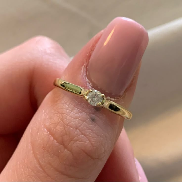 a close up of a person's hand holding a ring with a diamond on it