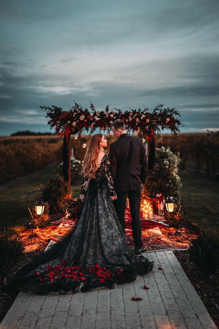 a man and woman standing in front of a wedding arch with flowers on the ground