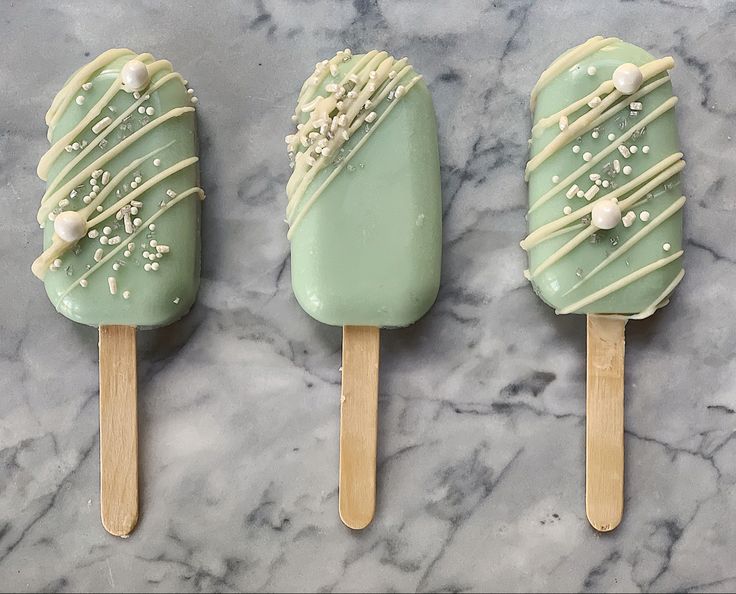 three popsicles with green frosting and sprinkles on them sitting on a marble surface