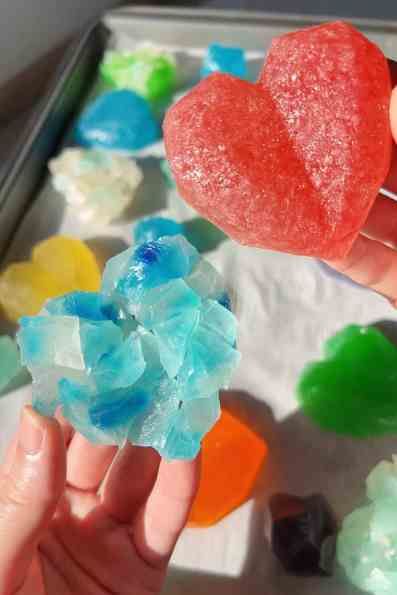 a person holding up a heart shaped lollipop in front of some gummy bears