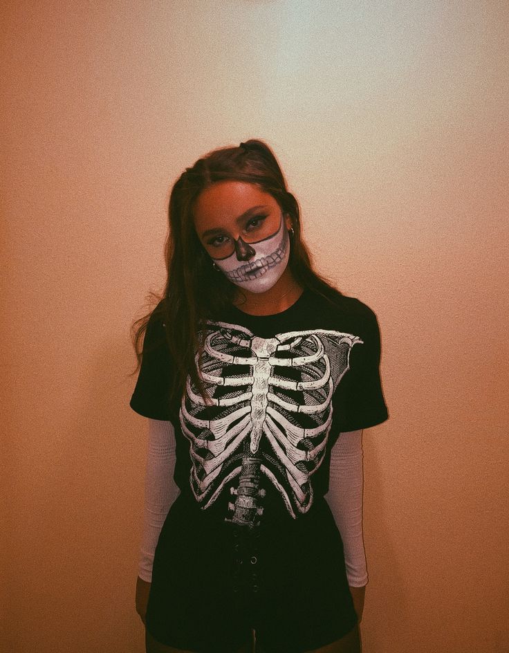 a girl with skeleton makeup on her face and black t - shirt, standing in front of a wall