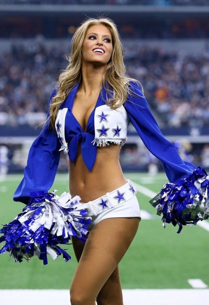 a beautiful woman in a cheerleader outfit standing on the sidelines at a football game