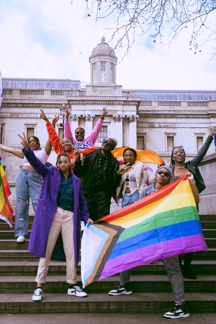 a group of people standing on the steps with their arms in the air and one holding a rainbow flag