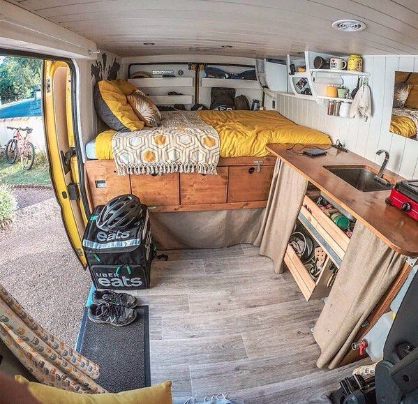 the interior of a camper van with bed, desk and storage area in it