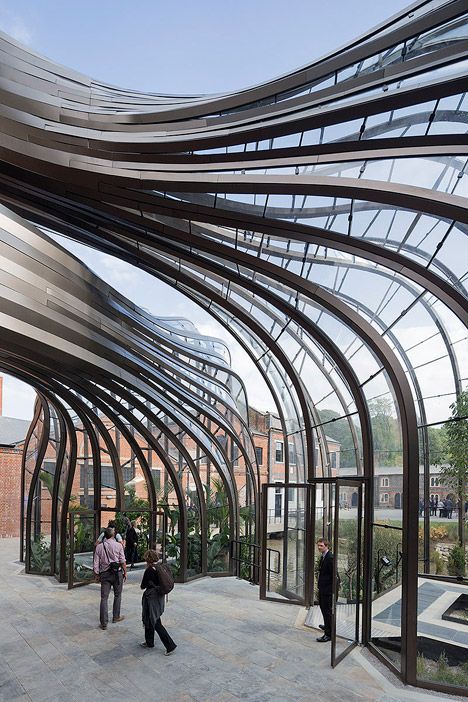 people are walking around in an open area with glass walls and curved metal structures on either side