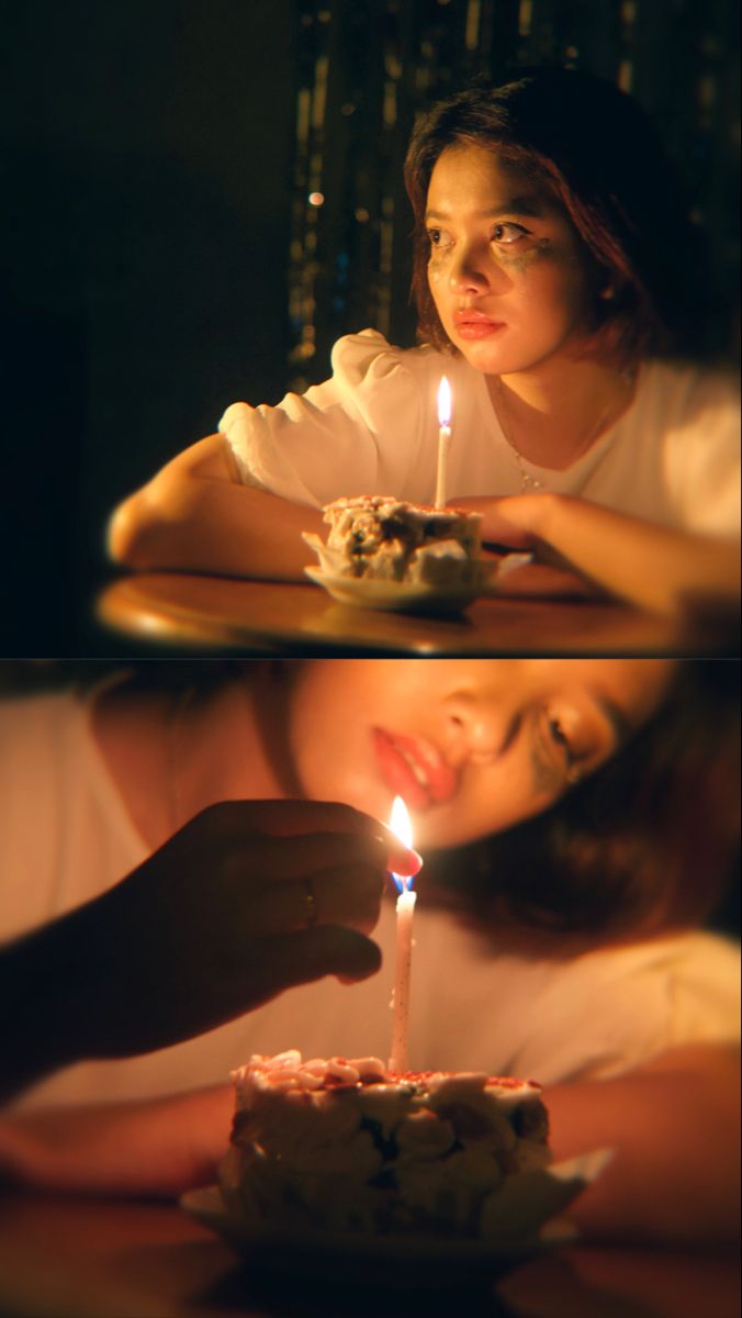 a woman sitting at a table with a cake in front of her and a lit candle on top of it