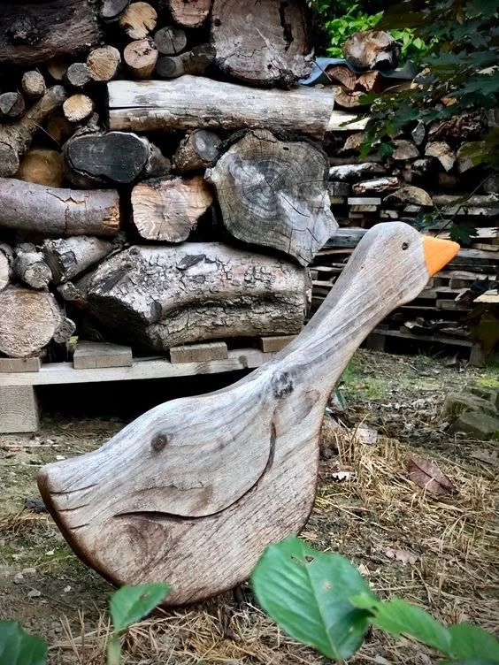 a wooden duck statue sitting in front of a pile of firewood and wood logs