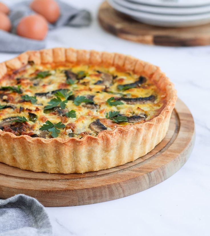 a quiche on a wooden platter with eggs in the background