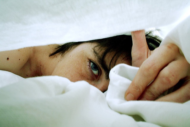 a close up of a person laying in bed under a blanket with their hand on the pillow