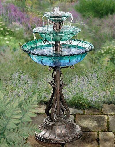 a three tiered glass fountain in the middle of a garden