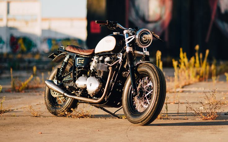 a black and white motorcycle parked on the side of a road next to weeds in front of a train track