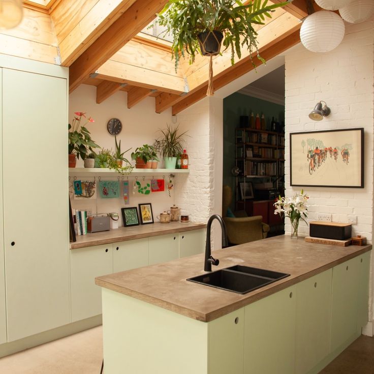 a kitchen with green cabinets and an island in the middle is decorated with potted plants