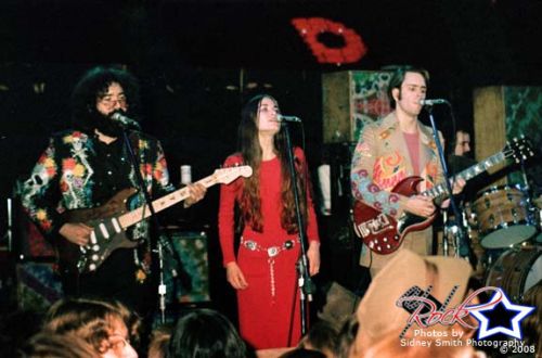 three people on stage playing guitars and singing