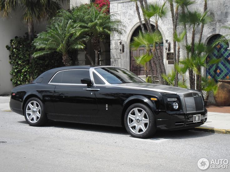 a black rolls royce parked in front of a building with palm trees and potted plants