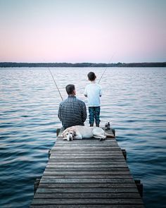 a man and child fishing from a dock with a dog sitting on the dock next to them