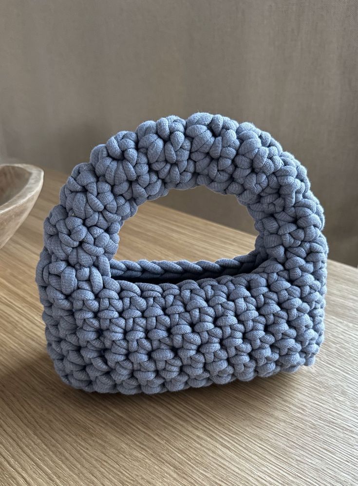 a blue knitted object sitting on top of a wooden table next to a bowl