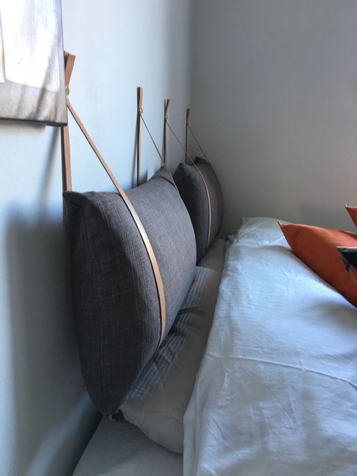 a bed with two pillows on top of it and an orange pillow in the corner