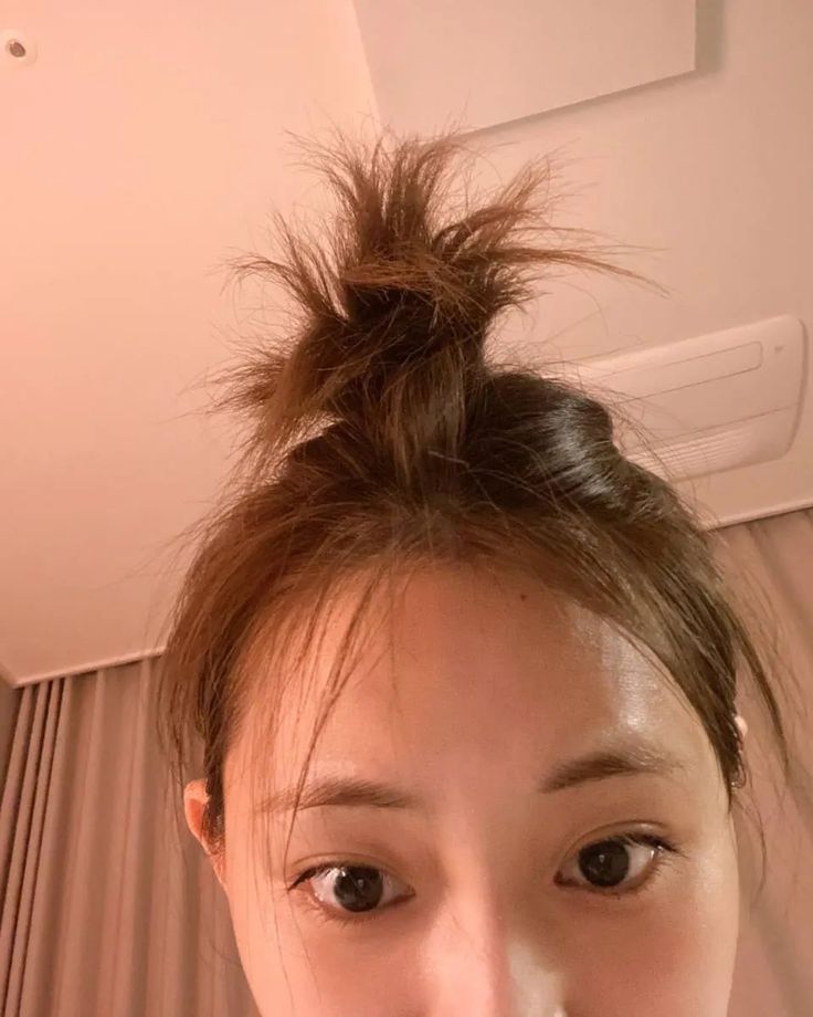 a woman with a messy topknot is taking a selfie