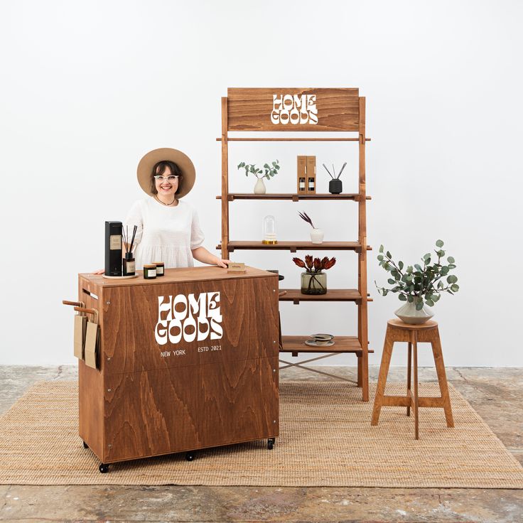 a woman standing behind a counter in front of some shelves with books and plants on it