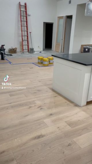 an empty room with hard wood flooring and white cabinets in the middle, while workers are working on the walls