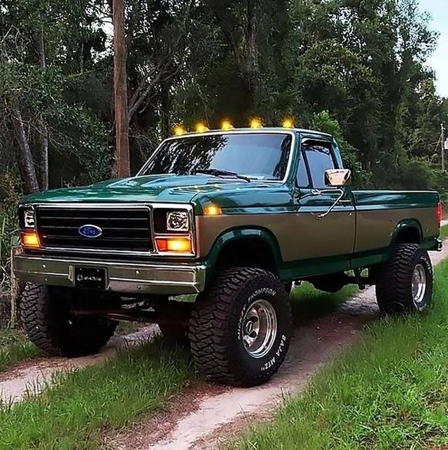 a green pick up truck parked on the side of a road next to a forest