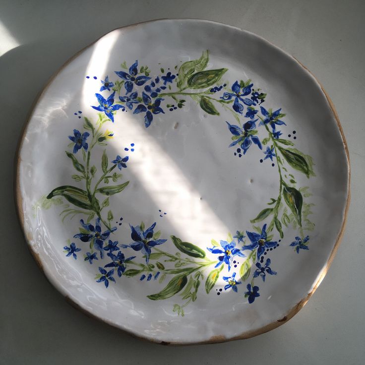 a white plate with blue flowers painted on the side and green leaves in the middle