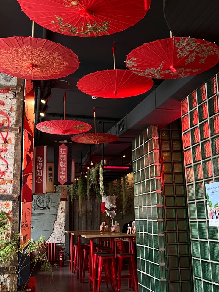 several red umbrellas hanging from the ceiling in a room with tables and stools