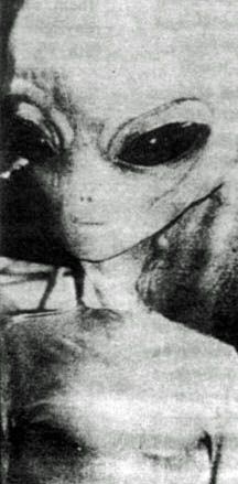 black and white photo of an alien with large eyes looking at the camera from behind