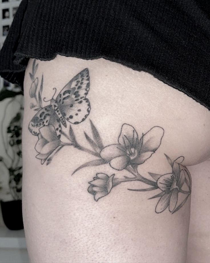 a woman's thigh with flowers and a butterfly tattoo on her side, which is black and white