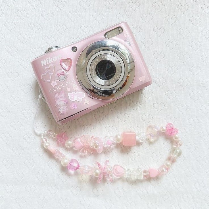 a pink digital camera sitting on top of a white table next to a beaded necklace