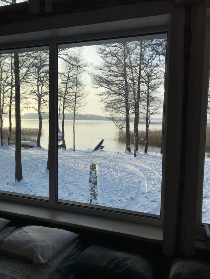 an open window with snow on the ground and trees in the background, looking out onto a body of water