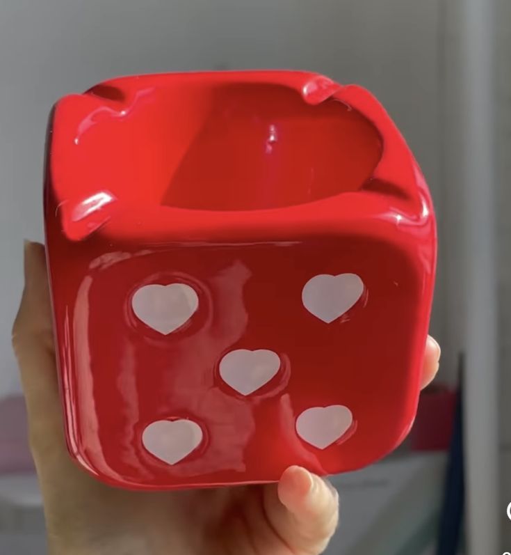 a hand holding a red plastic dice with hearts on it