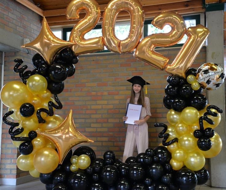 a woman holding a piece of paper in front of a graduation balloon arch with balloons