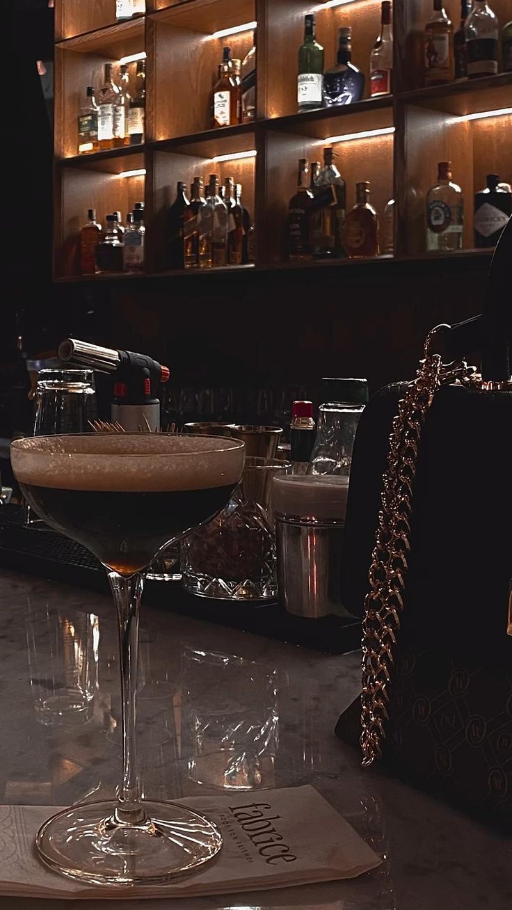 a martini glass sitting on top of a table next to a purse and liquor bottles