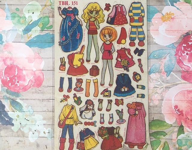 an assortment of paper dolls on a wooden surface with flowers and leaves in the background