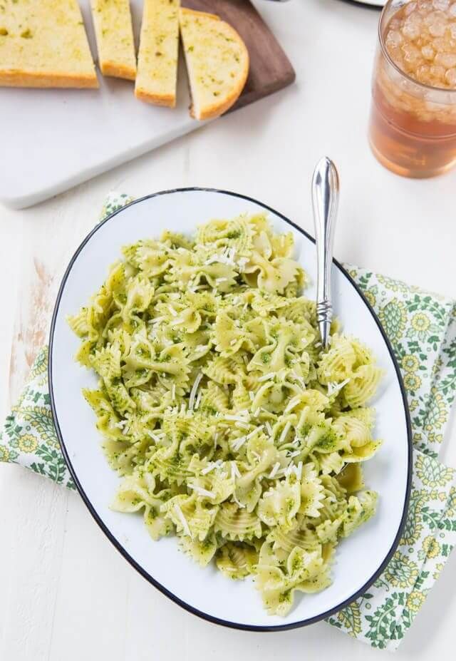 a white plate topped with pasta and pesto sauce next to slices of bread on a cutting board