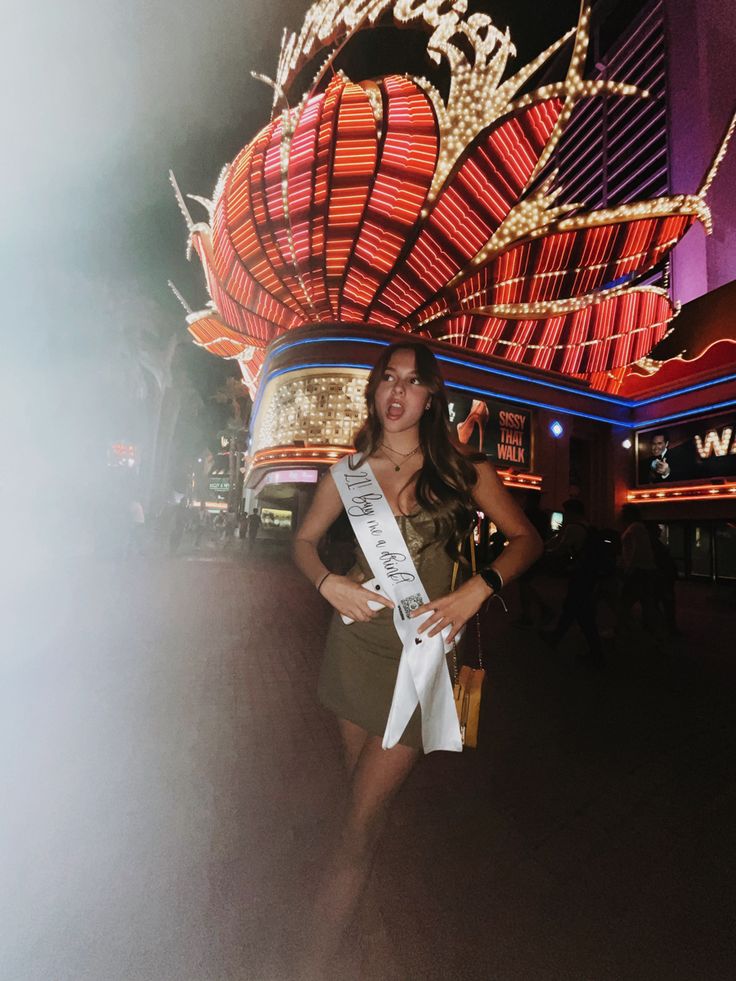 a woman standing in front of a building with a sash around her waist and wearing a tiara