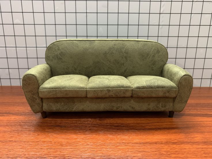 a green couch sitting on top of a wooden floor next to a white tiled wall