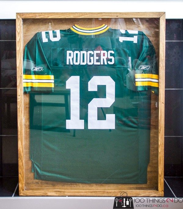 the green bay packers jersey is displayed in a wooden frame on a black tile wall