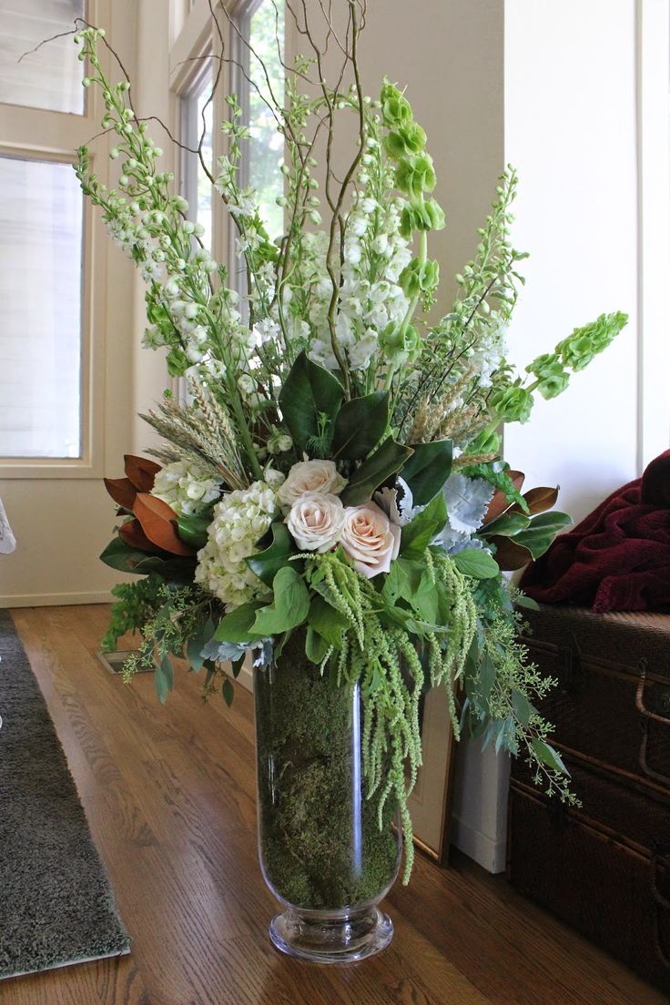 a vase filled with lots of flowers on top of a hard wood floor next to a window