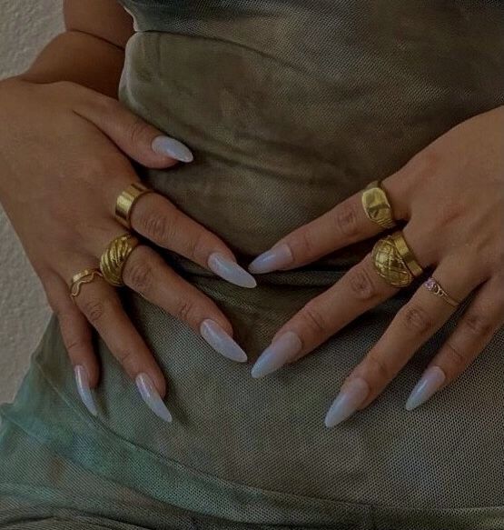 a woman with white nails and gold rings on her hands, standing in front of a wall