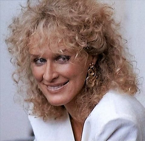 a woman with blonde hair smiling at the camera while wearing earrings and a white jacket