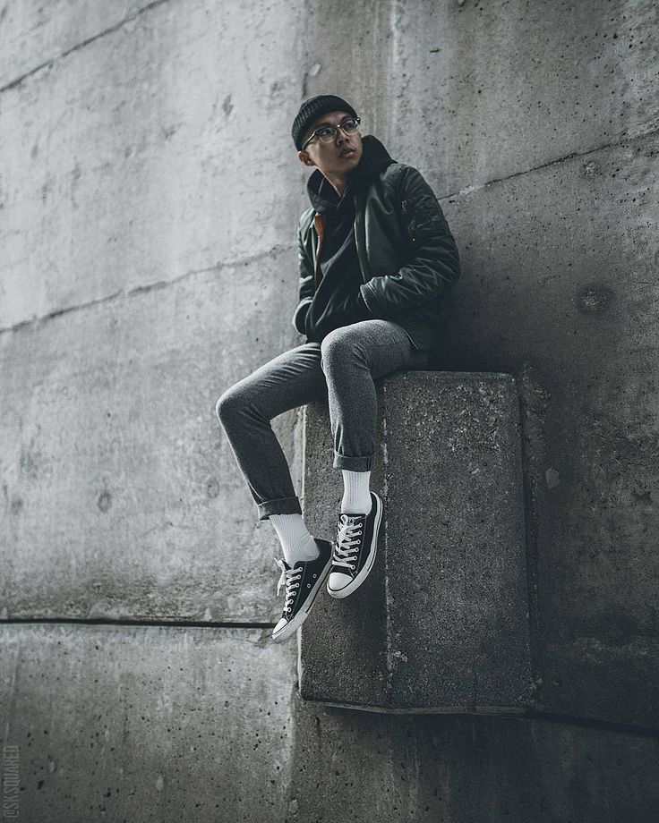 a man sitting on top of a cement block next to a wall with his hands in his pockets