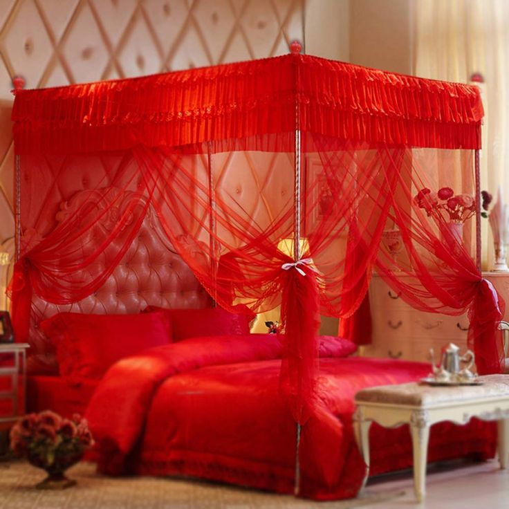 a bed with red sheets and curtains in a room