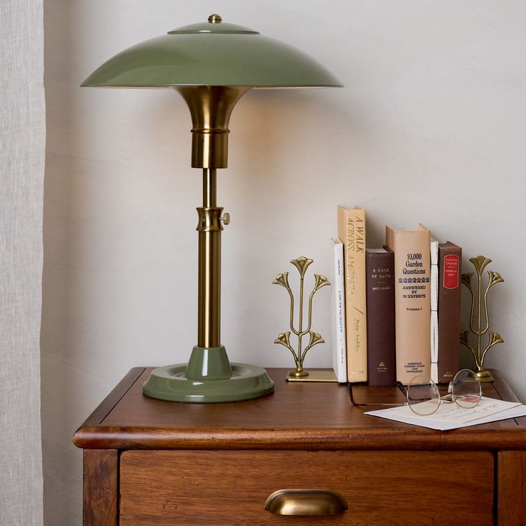 a green lamp sitting on top of a wooden table next to books and an open book